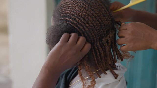 Closeup of braided hair styling. Professional stylist perfects intricate braid details. An experienced senior stylist carefully applies final touches to elegant braided hairstyle preparedness
