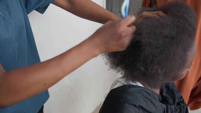 Hair comb closeup showing stylist detangling natural afro texture, client seated in protective cape, hands gently working through coils, calm indoor light, careful scalp care, slow precise technique