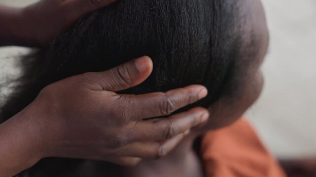 Hands combing woman natural hair, gentle detangling at nape, warm indoor light with orange blouse, fingers smoothing strands, preparation for style, intimate caregiving moment, calm domestic routine,