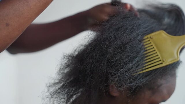 Tight hair detangling with yellow pick and tail parting, stylist performs precise sectioning and brisk combing active salon session, visible dust and frizz release, skilled technique, forearm motion