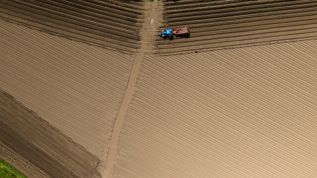 Aerial view of a blue tractor tilling a large agricultural field with precise parallel furrows Knottingley, England, United Kingdom.