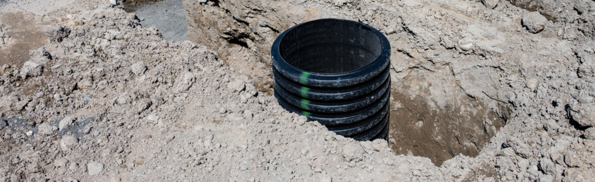 Septic Tank Riser, large black plastic corrugated pipe, installed in trench dug out in dirt of housing development construction project, site preparation detail earthwork
