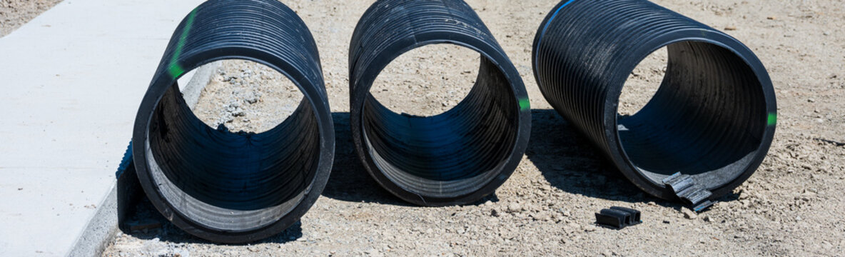 Septic Tank Riser, large black plastic corrugated pipe, sections ready for installation sitting on graded dirt ground
