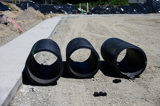 Septic Tank Riser, large black plastic corrugated pipe, sections ready for installation sitting on graded dirt ground
