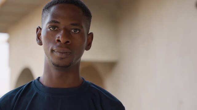 Black man portrait in corridor, young African male under arched walkway, subtle sweat on forehead, contemplative gaze and natural expression, soft sunlight creating warm tonal contrast, shallow depth