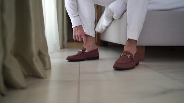 Man prepares himself for formal event by putting on brown loafers carefully