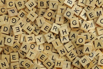 Pile of wooden tiles with various letters in big amount scattered on white board, closeup view © Larysa