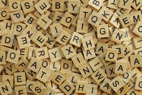 Pile of wooden tiles with various letters in big amount scattered on white board, closeup view
