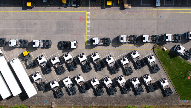 Aerial view of rows of white semi-truck cabs parked in a logistics distribution center with asphalt ground and yellow markings Doncaster, England, United Kingdom.