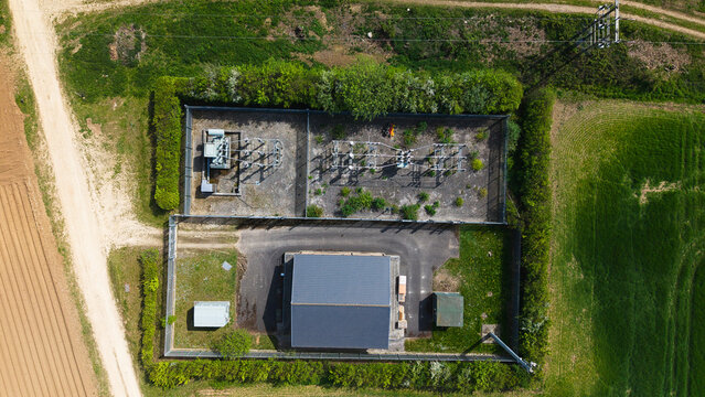 Aerial view of an electrical substation with transformers and power infrastructure surrounded by green hedges and agricultural fields in Hampole, England, United Kingdom.