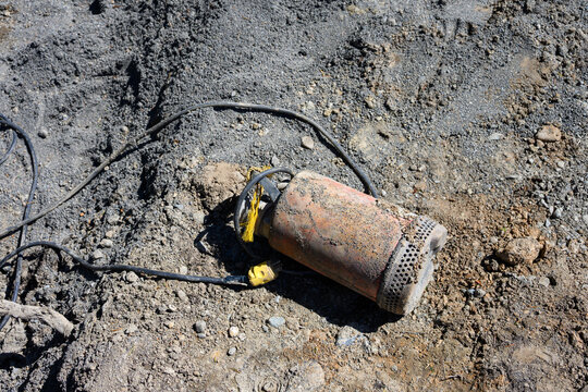 Submersible pump with power cord used to pump water out of trenches dug on construction site, laying on ground ready to use
