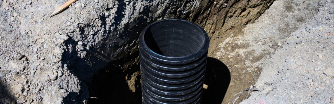 Septic Tank Riser, large black plastic corrugated pipe, installed in trench dug out in dirt of housing development construction project, site preparation detail earthwork
