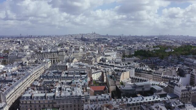 Aerial drone footage panorama of Paris city, shot under a partly cloudy sky. Densely built cityscape with rooftops in the foreground