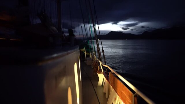 Cinematic night POV from the deck of the schooner Amazone as it navigates the dark, calm waters of the Beagle Channel, with the silhouetted Andes Mountains of Tierra del Fuego in the background