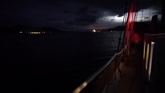 Cinematic night POV from the deck of the schooner Amazone as it navigates the dark, calm waters of the Beagle Channel, with the silhouetted Andes Mountains of Tierra del Fuego in the background