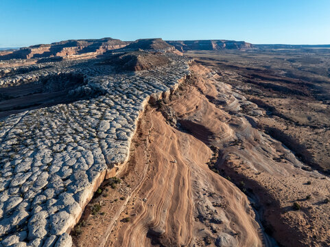 Aerial view of unique white rock formations and layered sandstone cliffs under a clear blue sky.
