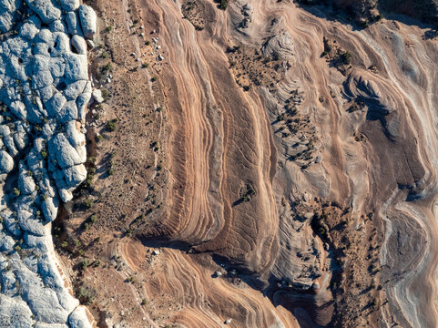 Aerial view of swirling sedimentary rock layers and textured white sandstone formations in a vast desert landscape.