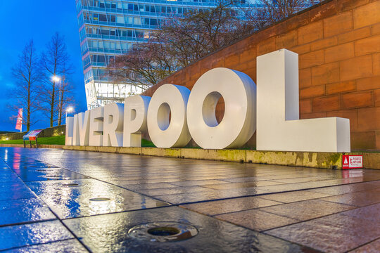 The large Liverpool city sign at Chavasse Park in the Liverpool ONE shopping district, illuminated during the blue hour on a rainy evening