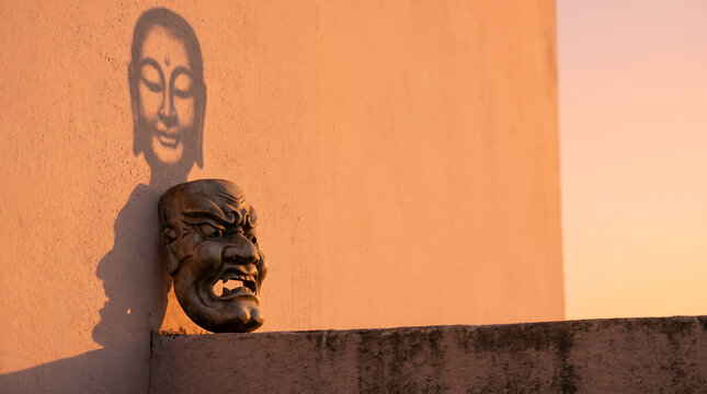 Hidden emotion: fierce mask, serene shadow on a sunlit wall, offering copy space for advertising and news.