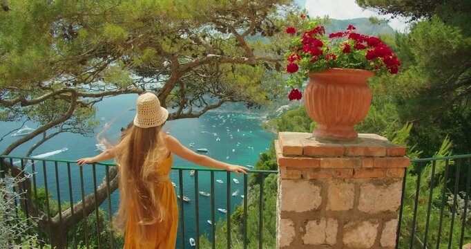 Long haired woman in dress admires Capri bay from cliff terrace on summer day