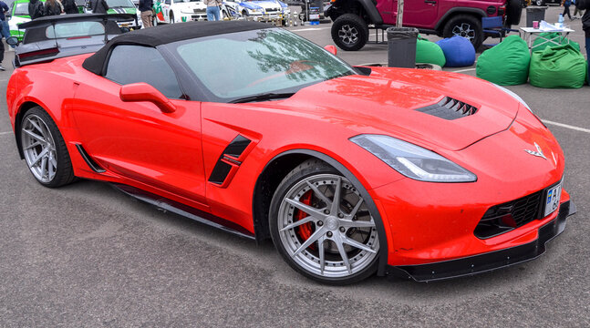 Bright red Chevrolet Corvette (C7) convertible with silver multi-spoke wheels and a black front splitter at outdoor event