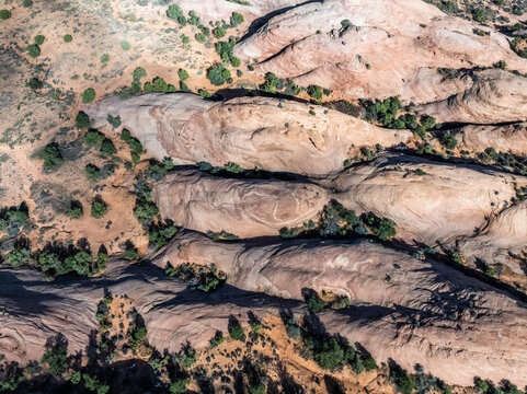 Aerial view of layered sandstone rock formations featuring unique swirling patterns and scattered green shrubs in an arid desert environment.