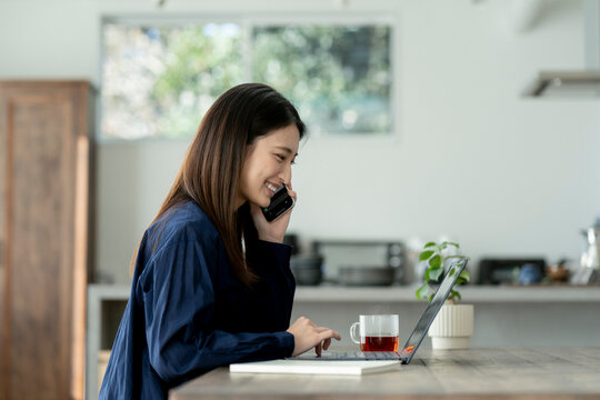 スマートフォンで通話しながらノートパソコンを見る若い日本人女性