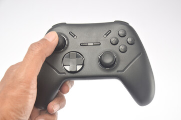 hand holding a black wireless gamepad controller isolated on a white background. Modern gaming hardware featuring dual analog sticks, directional pad, and action buttons for console or pc. © Setyotuhu