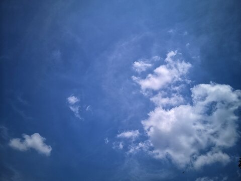 This photo shows a view of a clear blue sky. There is a formation of white clouds that are quite thick and lumpy (cumulus clouds) on the right side. In the middle, there are thin clouds that float 
