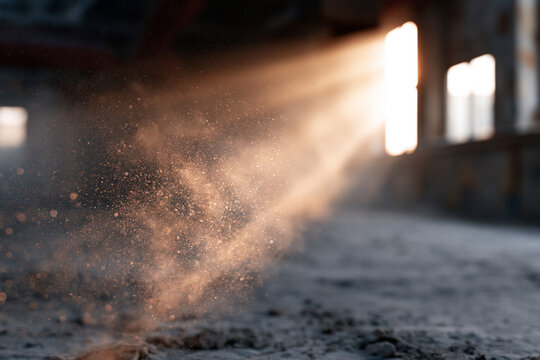 Dust particles swirl in sunlit beams across an empty, gritty floor. Sunlight pierces the haze from a distant window. The space feels abandoned, silent, and textured