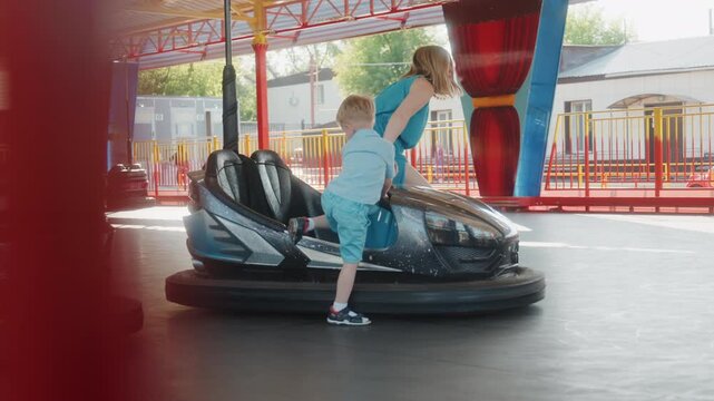 Child boarding bumper car at park, sunlit fairground scene with mother helping toddler into ride, colorful pavilion and gentle motion, candid smiles and bonding during weekend family outing