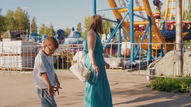 Exploring amusement park together. Mother and child meander through lively carnival rides in park. Relaxed family walk enjoying bright colors and exciting sights at weekend amusement area