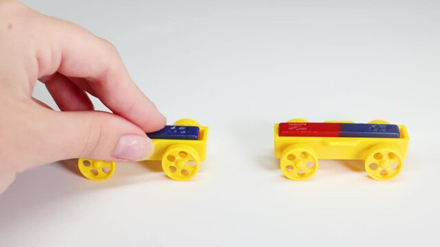 A close-up shot of a hand demonstrating magnetic repulsion and attraction with yellow toy trains on a pristine white surface.