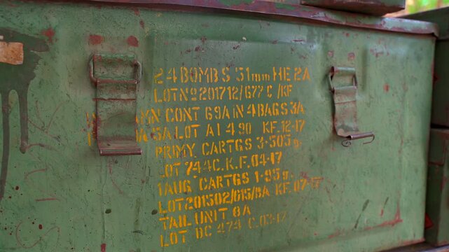 A close-up static shot of a weathered green metal ammunition crate featuring yellow stenciled military specifications and lot numbers, showing authentic rust and wear