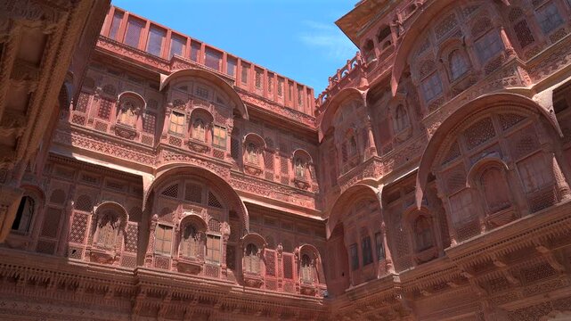 A low-angle static shot showcasing the stunningly detailed red sandstone facades and arched windows of the inner courtyard at Mehrangarh Fort in Jodhpur, Rajasthan, India