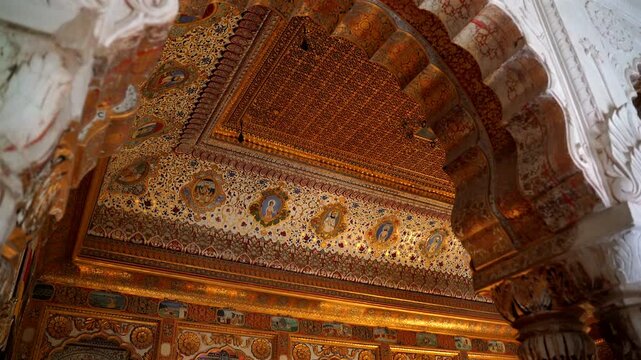 A static low-angle shot of the opulent Phool Mahal interior, showcasing the intricately painted gold leaf ceiling, decorative arches, and royal portraits in Mehrangarh Fort, Jodhpur, India
