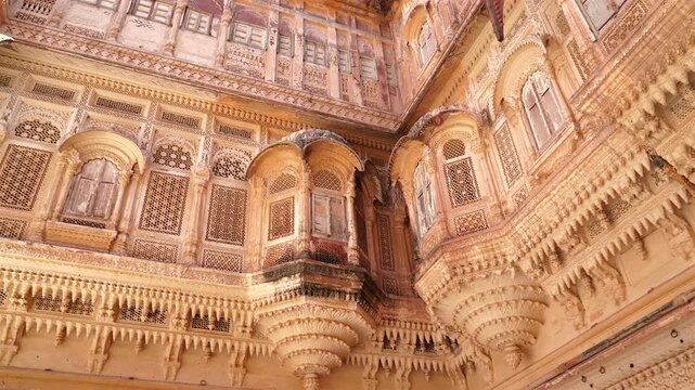 A static low-angle shot showing the exquisite stone craftsmanship of the Jharokha balconies and ornate facades within the palace complex of Mehrangarh Fort, Jodhpur, India
