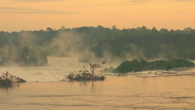 Golden sunrise light over Murchison Falls on the Nile River in Uganda with warm tones illuminating powerful water rushing through a narrow rocky gorge in Africa