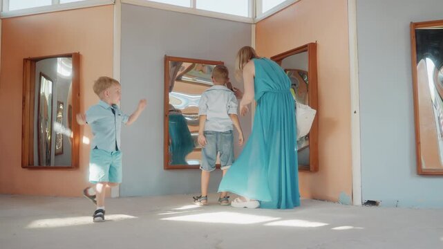 Mother guides two boys at mirror, white mother in teal dress encourages playful movement, kids run and pose in sunlit pavilion, reflective panels create multiples, lively family weekend energy