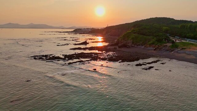 Cinematic dolly-in shot of dramatic rocky coastal cliffs bathed in warm golden sunset light, ocean waves below, moody sky. Ideal for travel, nature, and documentary projects.