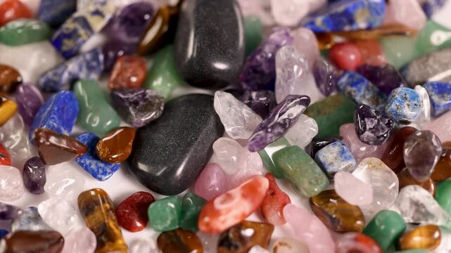 A close up view of colorful stones and minerals, some falling onto the pile, showcasing their diverse shapes, sizes, and vibrant hues.