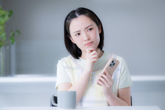 A portrait of a woman&mdash;perhaps a housewife&mdash;holding a smartphone, conveying the image of a Japanese consumer struggling with household budgets, rising prices due to inflation, and a strong yen, and grap