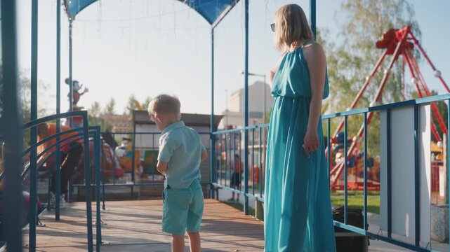 Family park activity. Women and child enjoying outdoor playtime. Mother and son sharing joyful moment at sunny park. Family outing captured with mother supervising young boy by playground rides