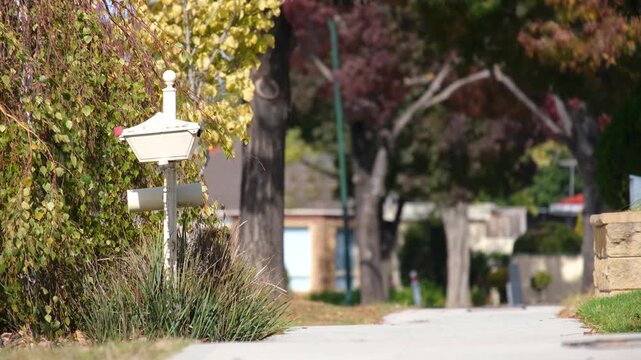 a classic white letterbox post&nbsp;on nature strip along a footpath at a quiet Australian suburban street.&nbsp;Blurred in the background are mature autumn trees in an established neighbourhood