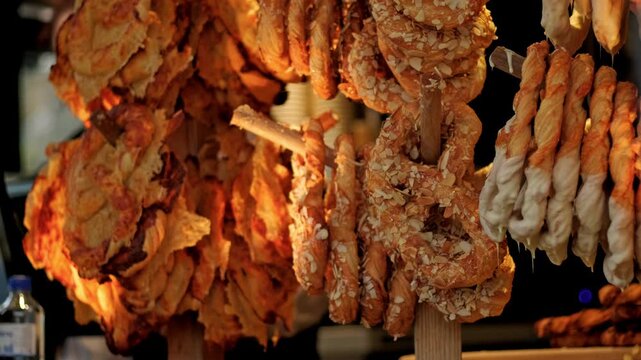 Golden pretzel hanging on wooden rack at market stall. Fresh baked pastry with almond and white glaze. Sweet snack product for Christmas fair shopping experience.