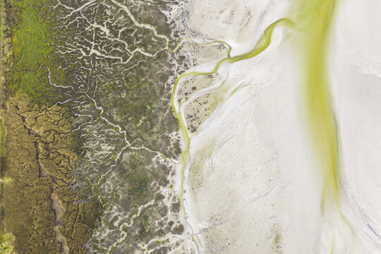 Aerial view of the intricate tidal patterns and winding water channels of a coastal salt marsh meeting the sandy beach Goulven, Brittany, France.