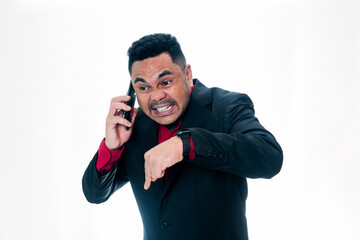 Naklejka premium Portrait of a furious businessman in a black suit shouting on a smartphone while pointing his finger down to the floor, isolated on a white background, representing authority, demanding presence, and 