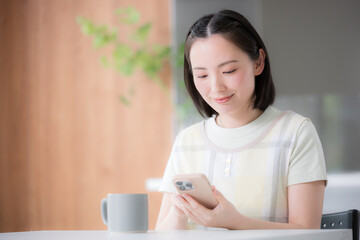 主婦のようなエプロンを着た女性　スマホを持ってタップする、検索や探す、口コミの投稿などキッチンやダイニングでくつろぐ © kapinon