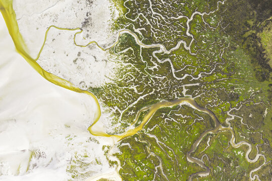 Aerial view of the intricate patterns of salt marshes with meandering water channels and green vegetation over white sandy flats in Goulven, Brittany, France.