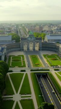 Vertical video. Brussels, Belgium. The Cinquantenaire monument, a triple triumphal gateway crowned by a bronze quadriga, framed by a sweeping colonnade and formal gardens, Drone footage under clear m